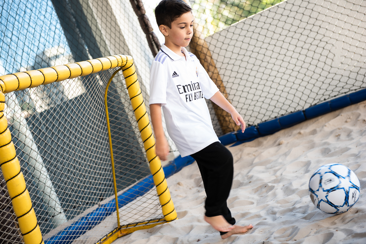 menino se preparando para chutar bola na quadra de futebol de areia