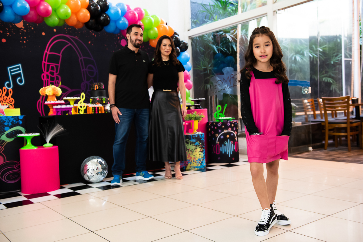 menina se destacando na foto com os pais aos fundos