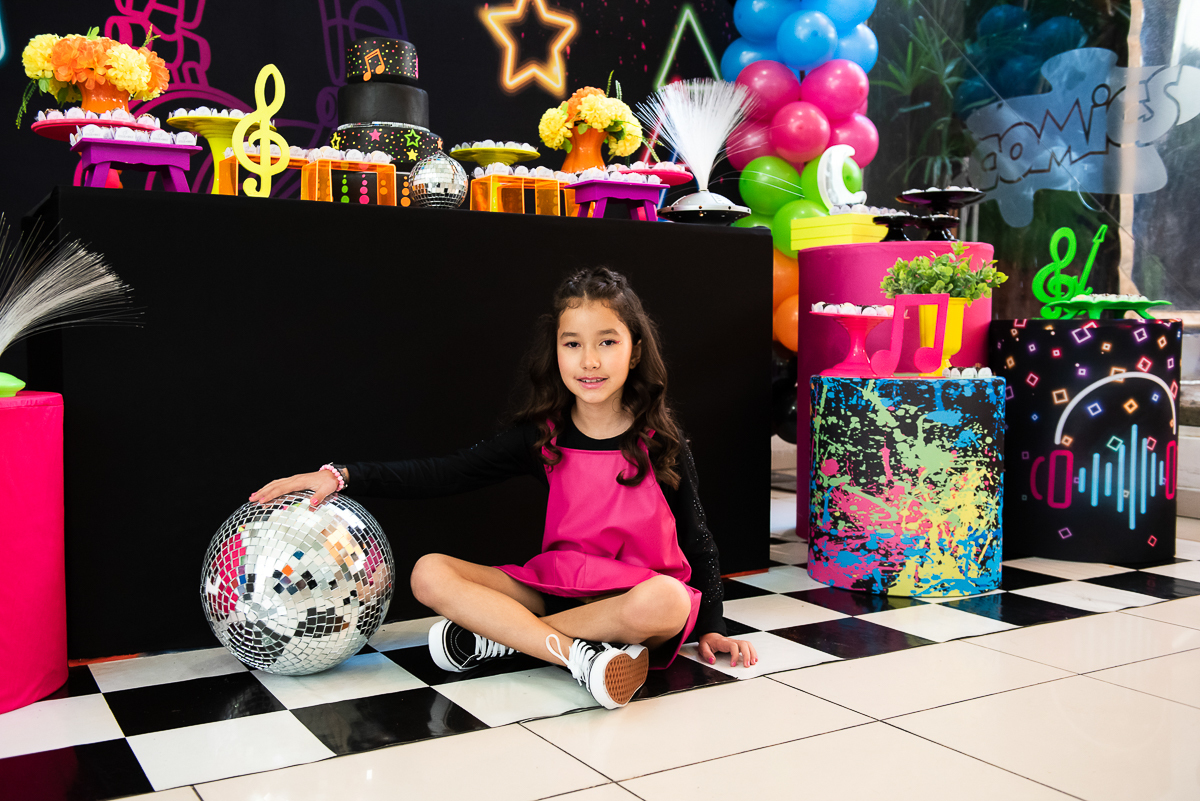 menina sentada curtindo a decoração da sua mesa de parabéns
