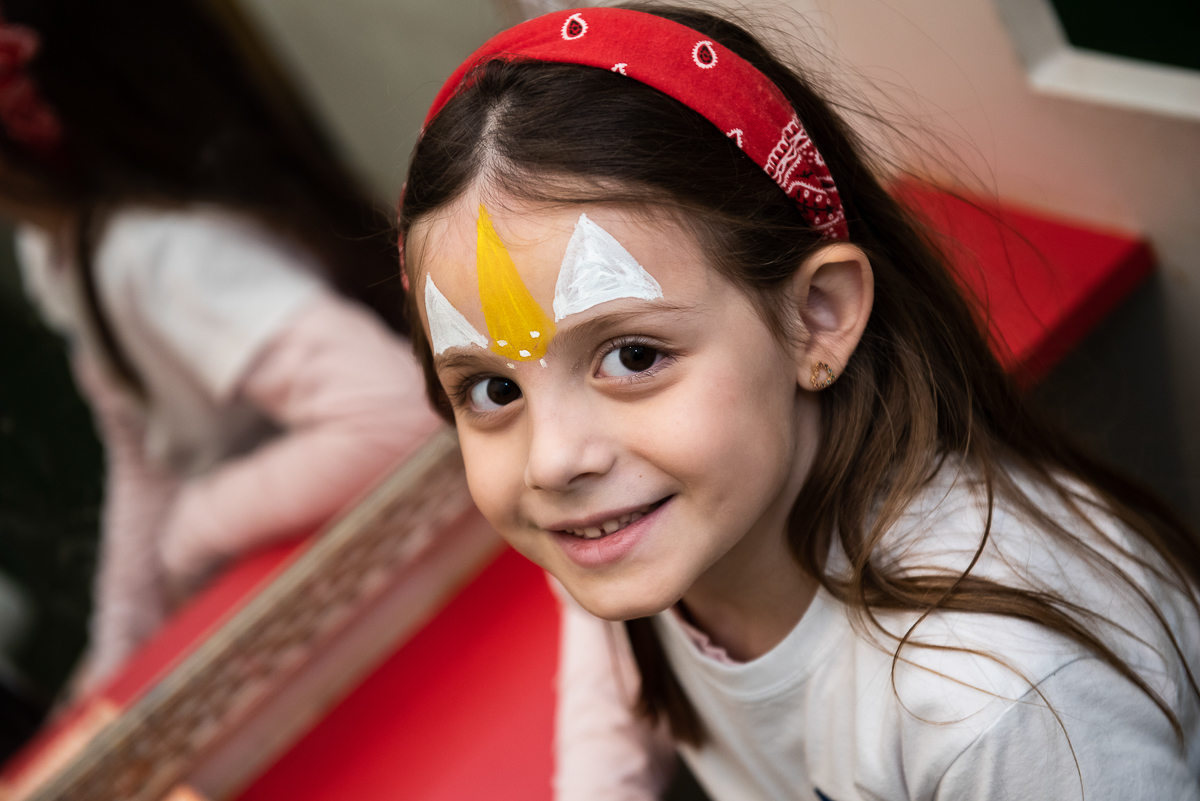 linda menina com maquiagem branca e amarela e tiara vermelha na cabeça