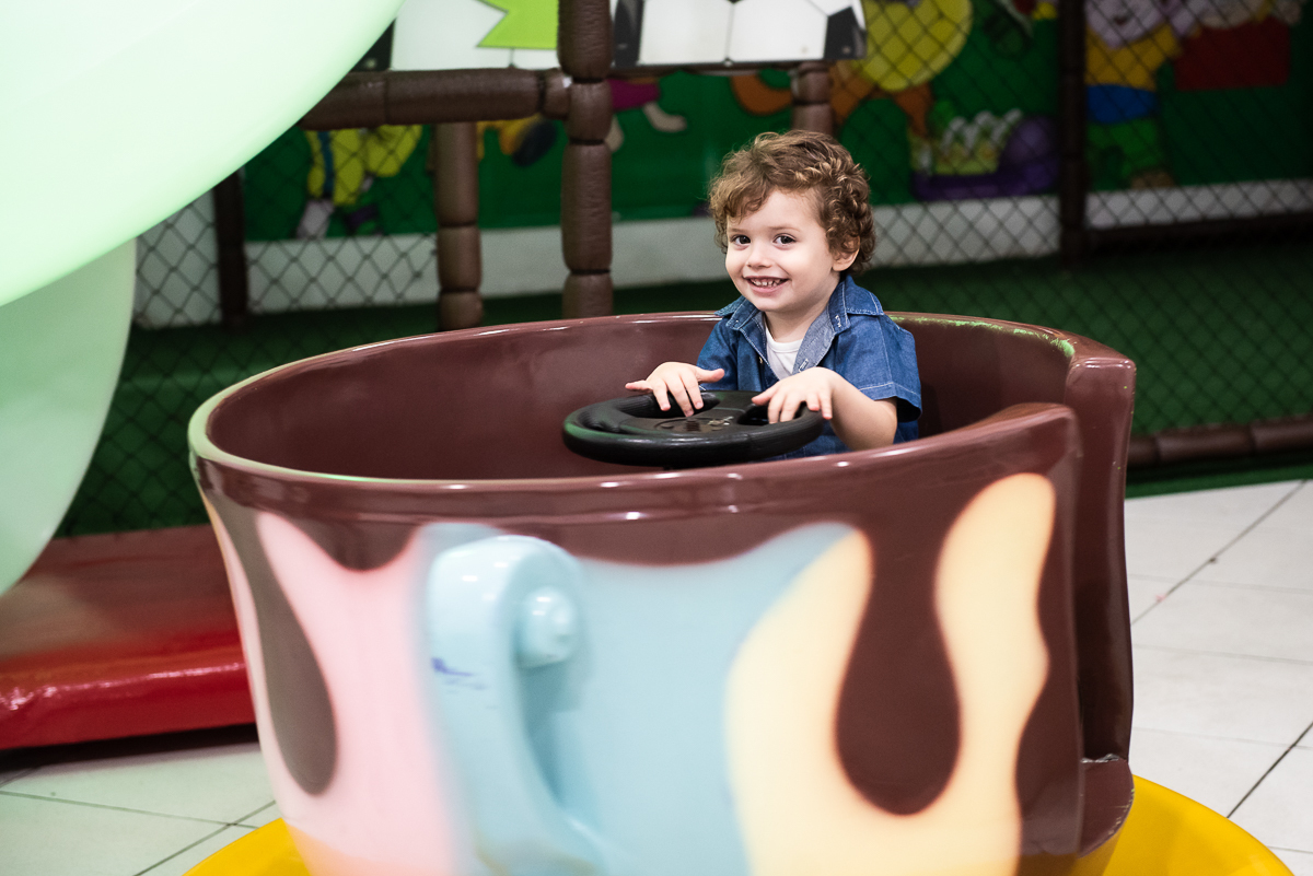 menino feliz dentro do brinquedo xícara do buffet