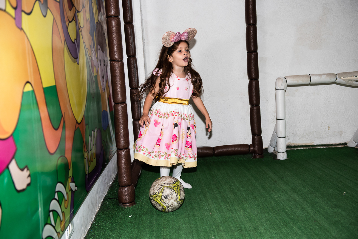 menina na quadra de futebol com a bola no pé