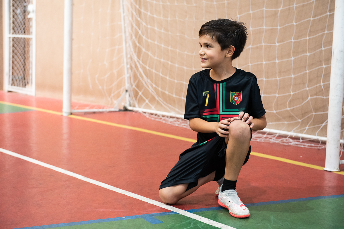 menino fazendo pose para fotografia na trave do gol
