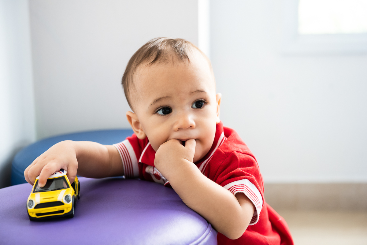 criança com dedo na boca e carrinho amarelo