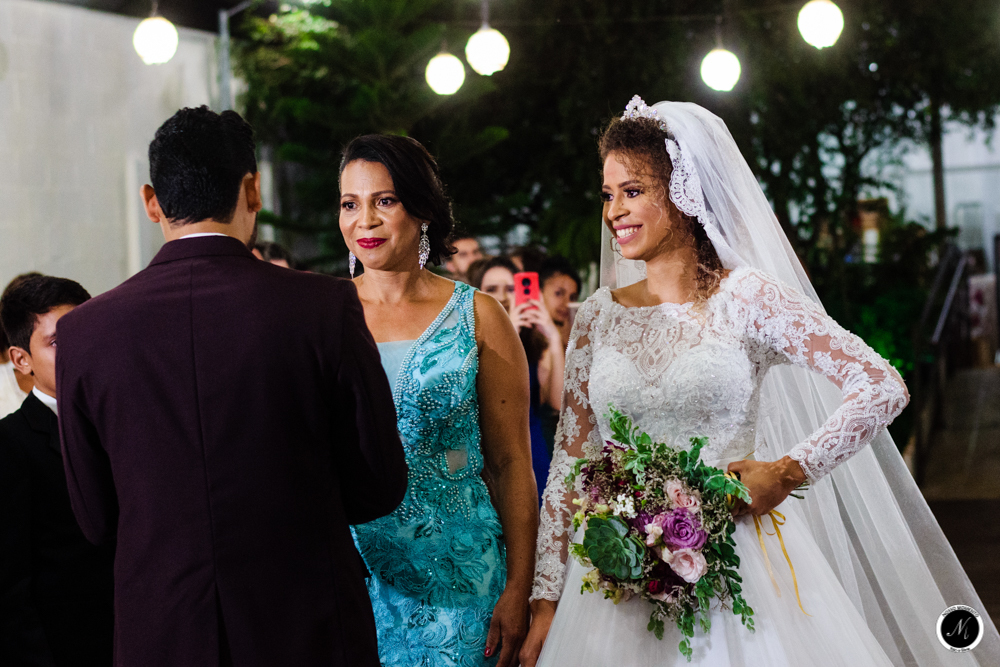 Noiva sorrindo ao ver seu noivo cumprimentar sua mae no casamento ao ar livre durante a noite