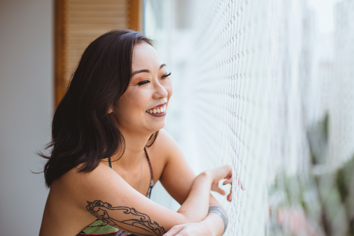 Ensaio feminino sensual em casa com mulher japonesa, Suzy e fotografa Dani Ortiz, com ela encostada na varanda da sala.