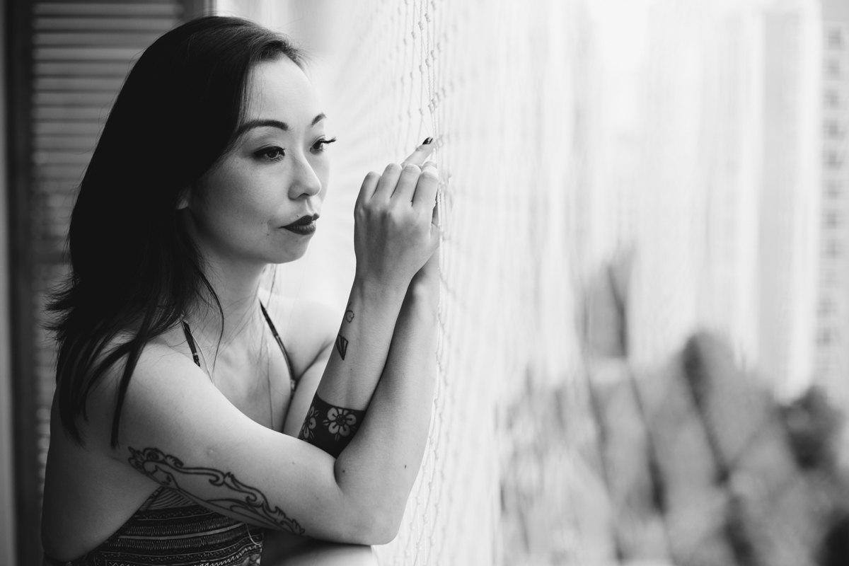 Ensaio feminino sensual em casa com mulher japonesa, Suzy e fotografa Dani Ortiz, com ela encostada na varanda da sala.