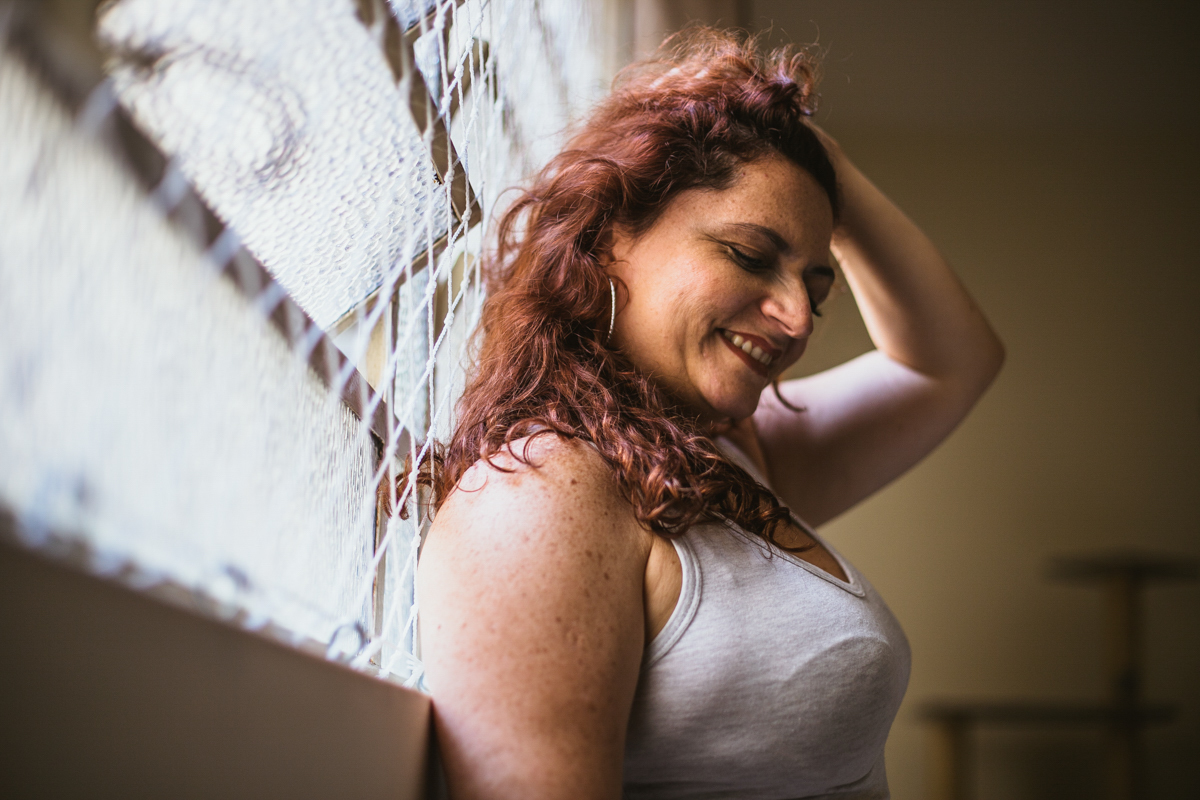 Usando regata básica no Ensaio feminino sensual em casa com mulher ruiva, Vivian e a fotógrafa Dani Ortiz no Ipiranga em São Paulo encostada na janela.