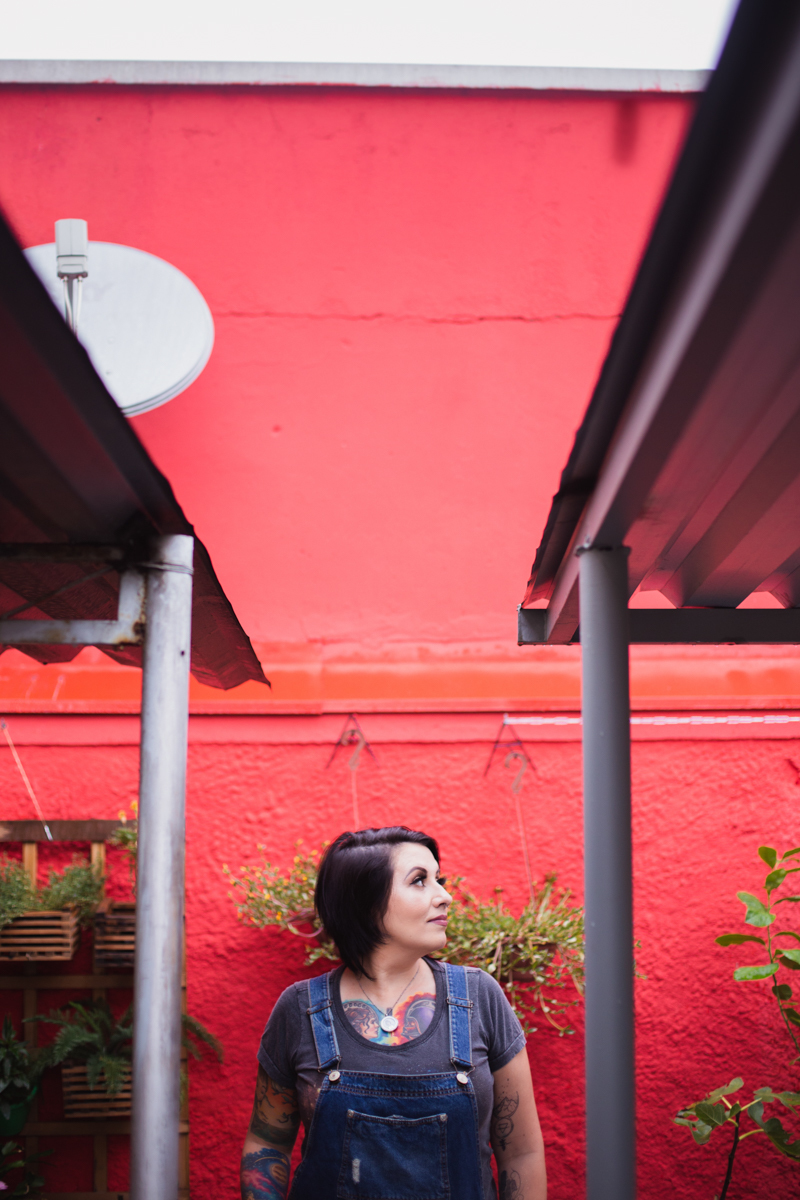 Parede vermelha no Ensaio feminino sensual em casa com mulher tatuada, Clau e fotografa Dani Ortiz.