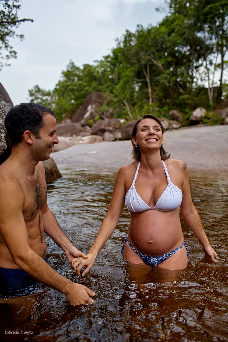casal entrando na água gelada da cachoeira em sessão fotográfica gestante