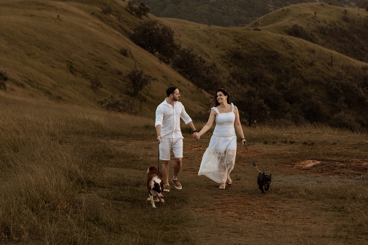 Casal em ensaio pré-wedding ao nascer do sol no Morro do Capuava, rodeado pela natureza e acompanhados por seus cachorros