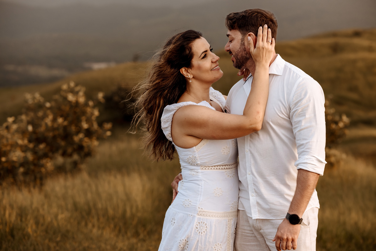 Ensaio pré-wedding romântico no campo, com casal trocando olhares apaixonados em meio à luz dourada da manhã