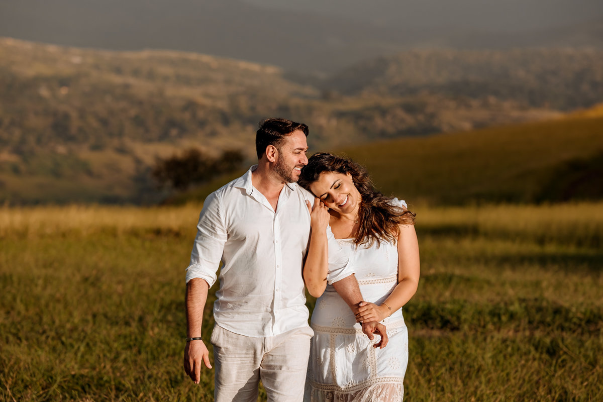 Ensaio pré-wedding romântico no campo, com casal trocando olhares apaixonados em meio à luz dourada da manhã