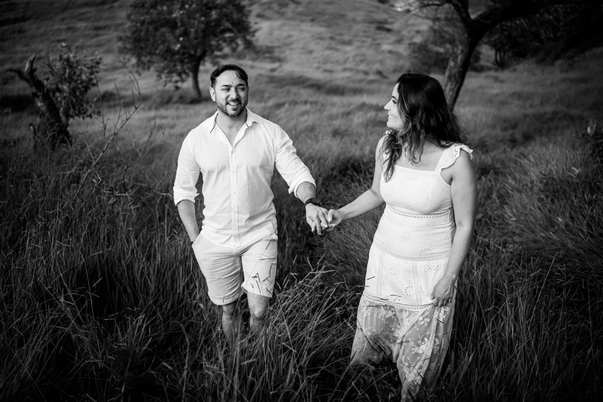 Ensaio pré-wedding romântico no campo, com casal trocando olhares apaixonados em meio à luz dourada da manhã