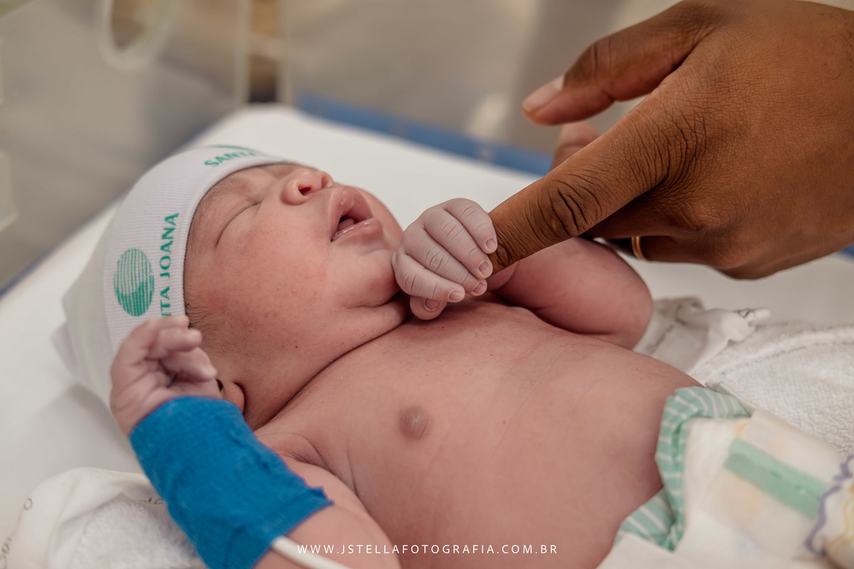 recém nascido segurando dedo do pai