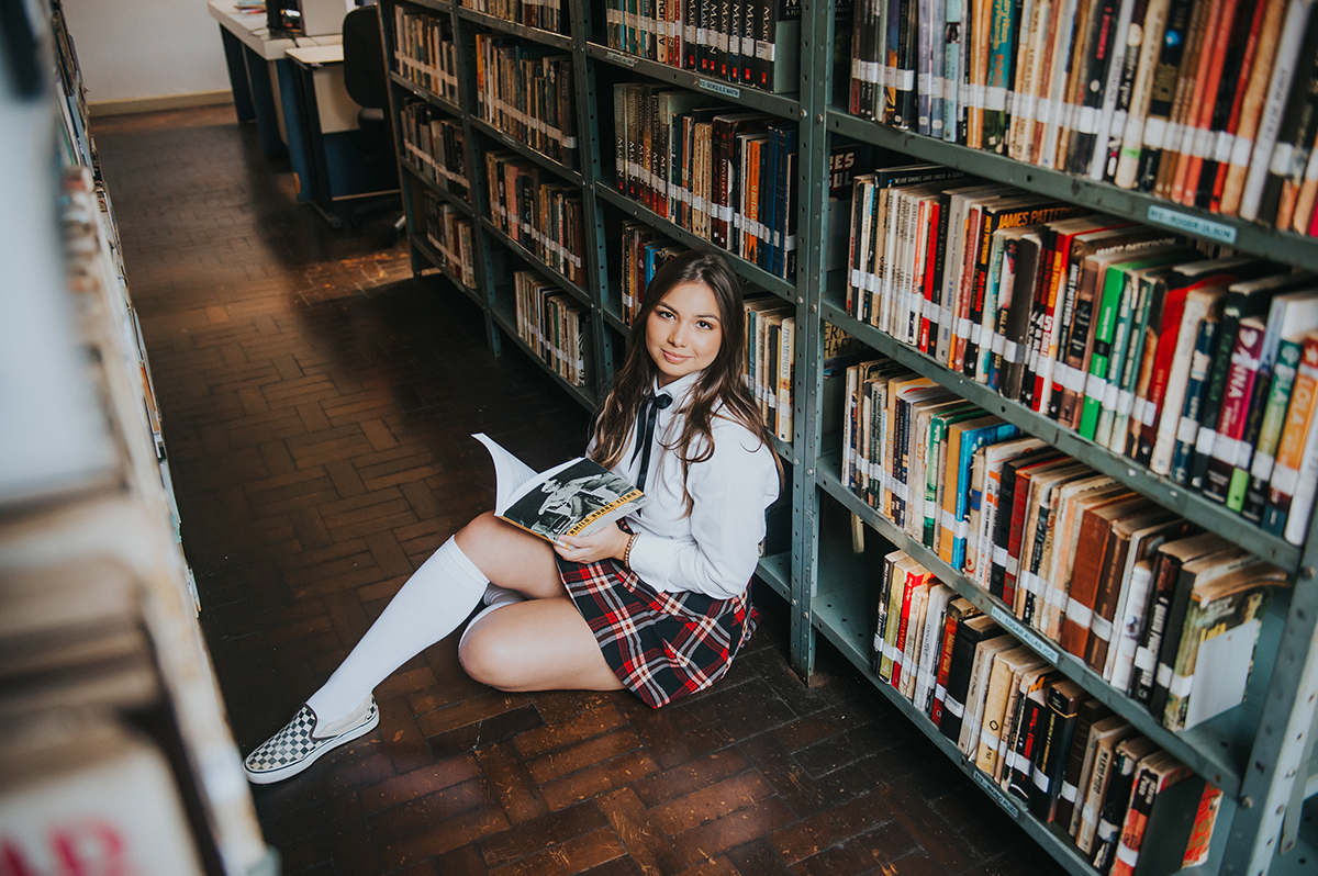 Debutante sentada no chão da biblioteca lendo um livro
