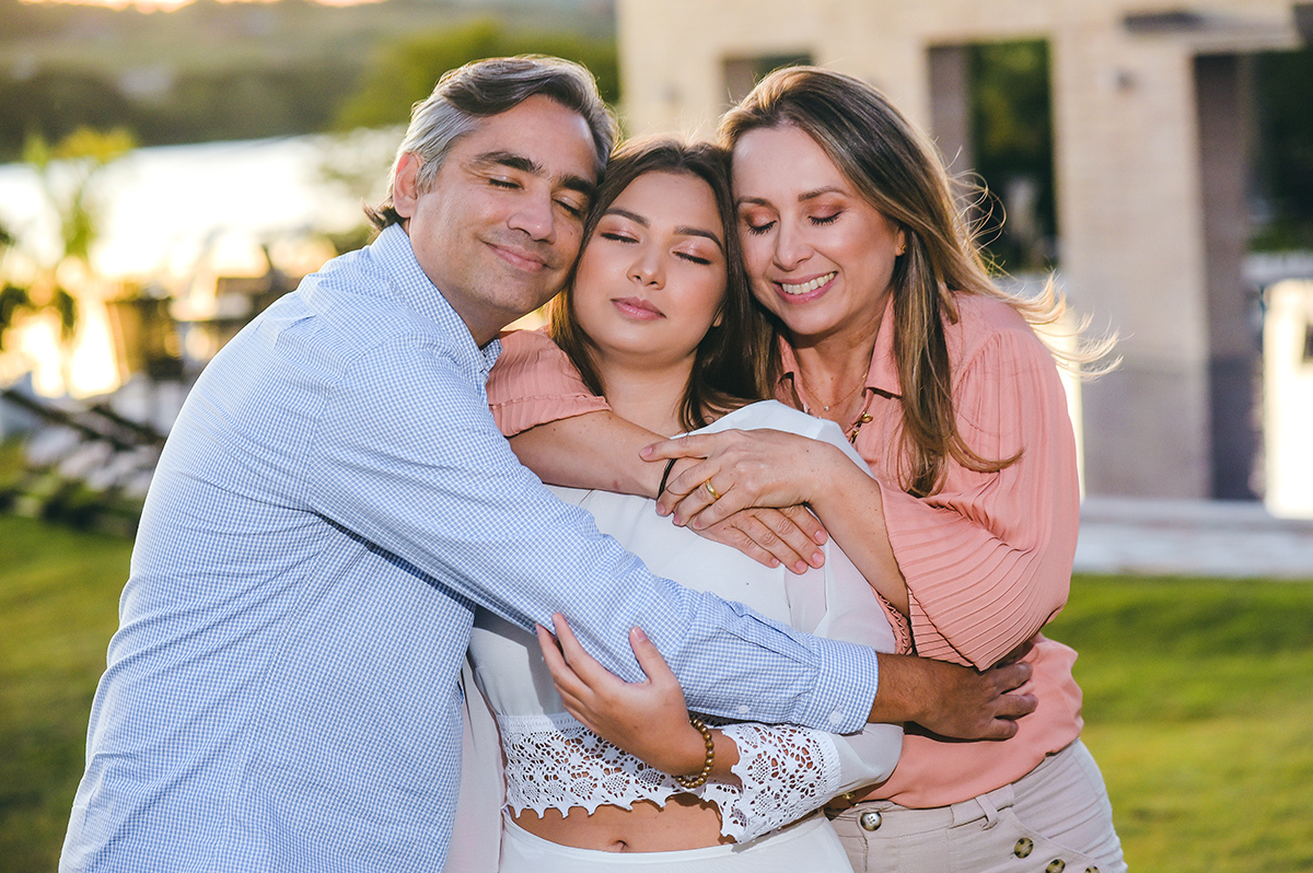 Pai e mãe abraçando na filha que comemora seus 15 anos