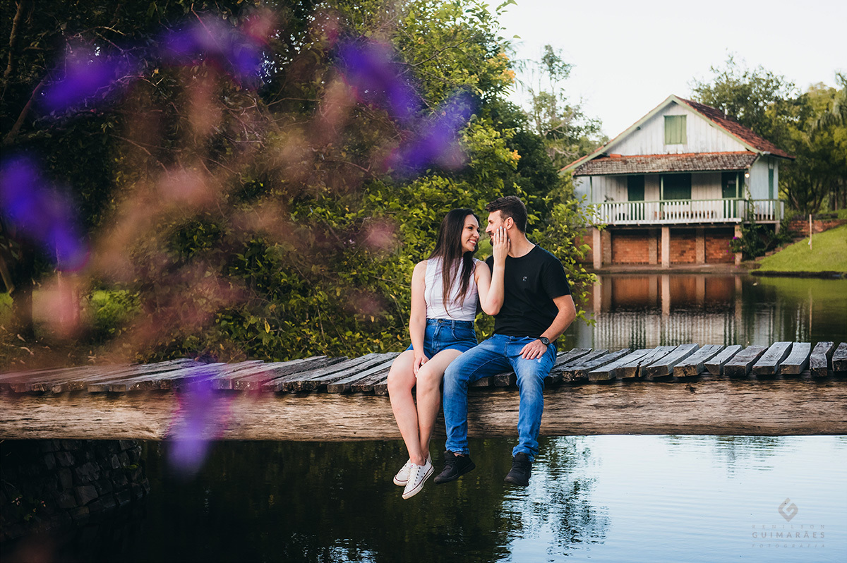 Foto do casal sentado em uma passarela no meio do lago