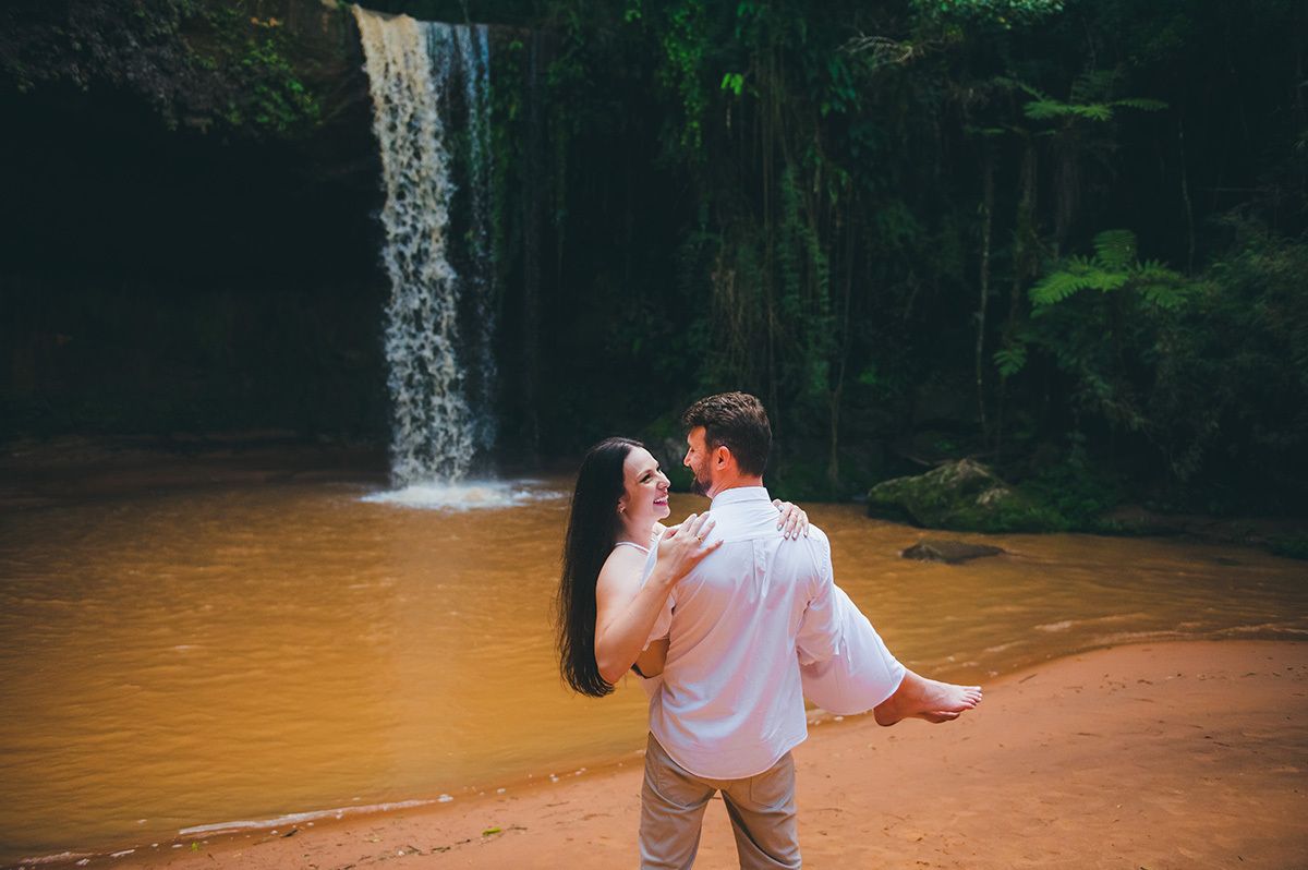 Noivo com a noiva no colo em frente a cachoeira
