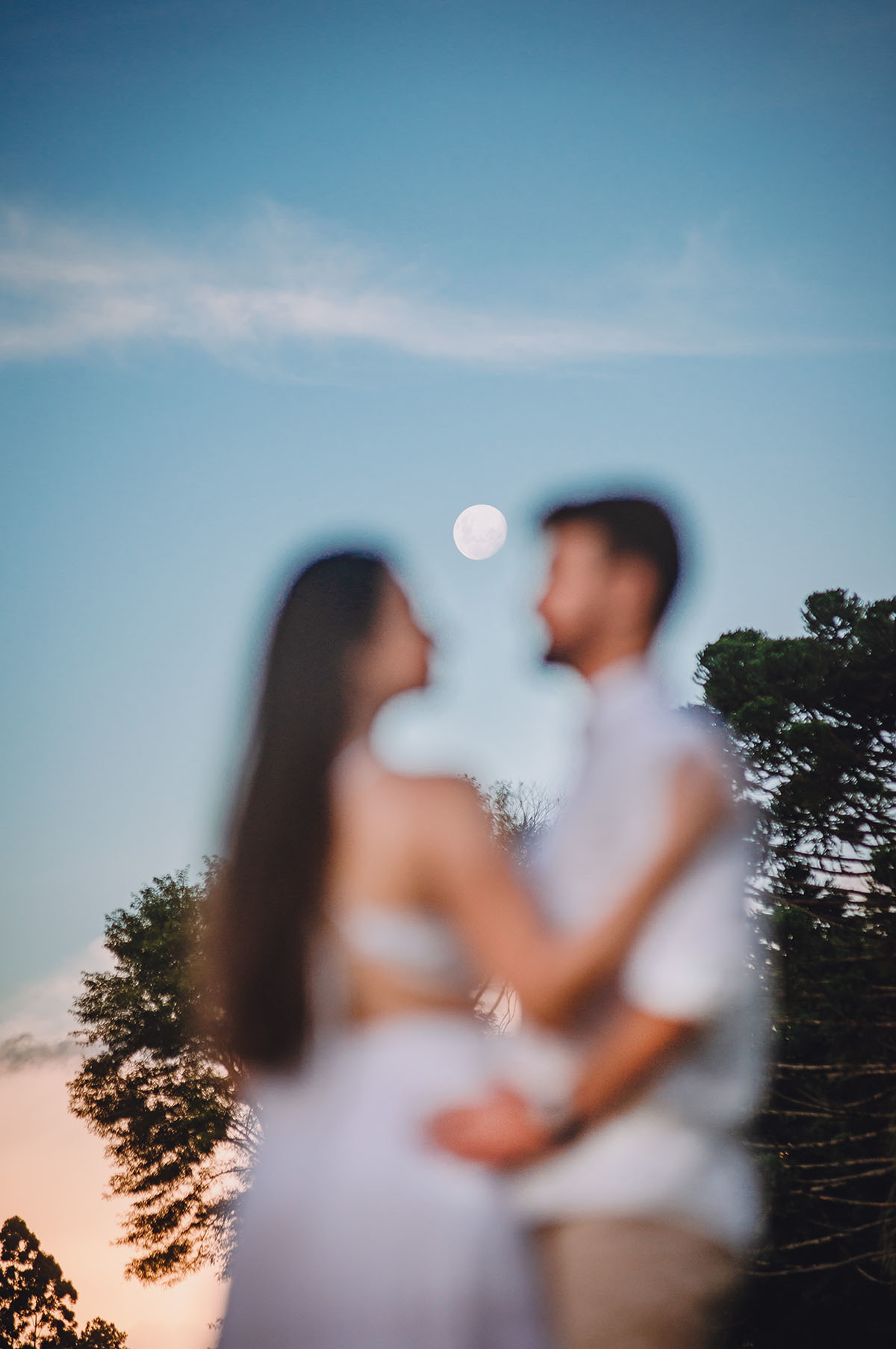 Foto do casal desfocado em primeiro plano e a lua focada em segundo plano