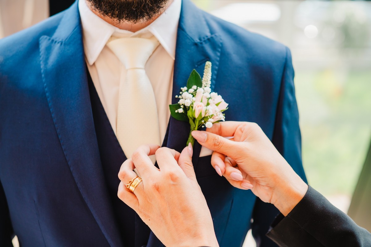Mãos da assessora colocando a flor no terno do noivo