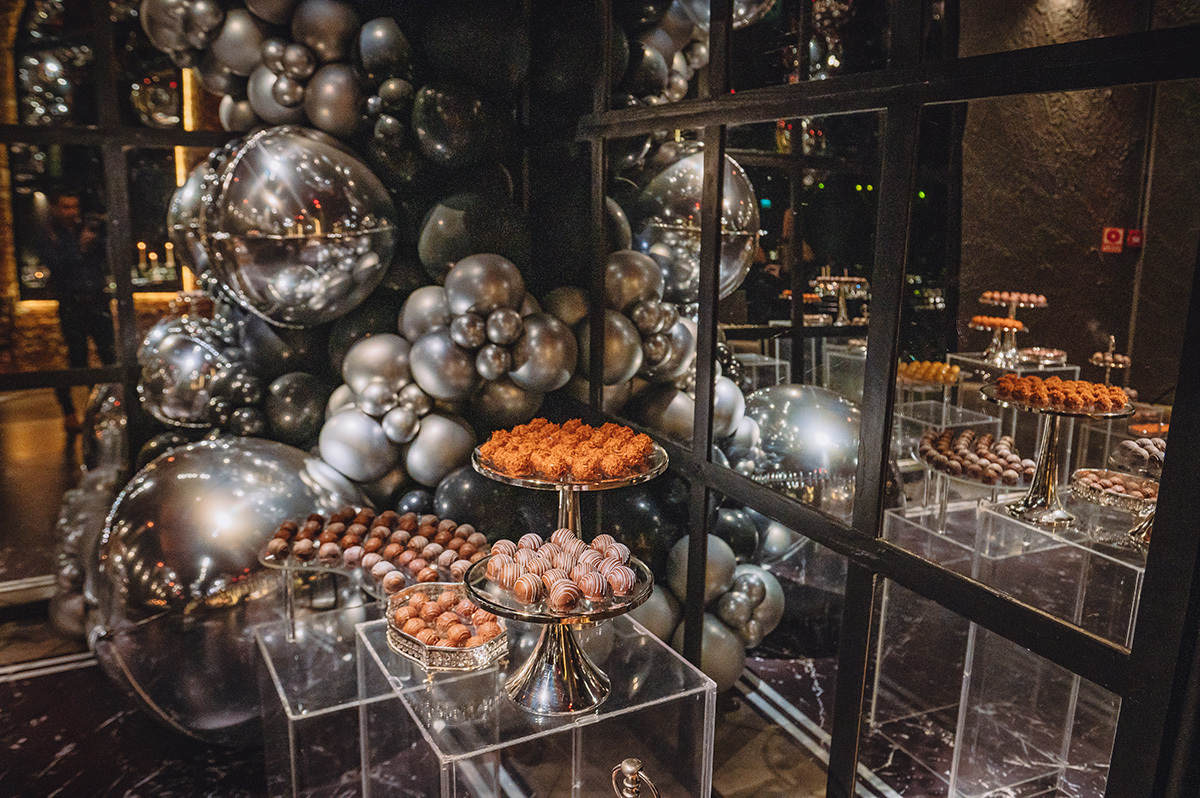 Foto da mesa de doces com balões prata atrás