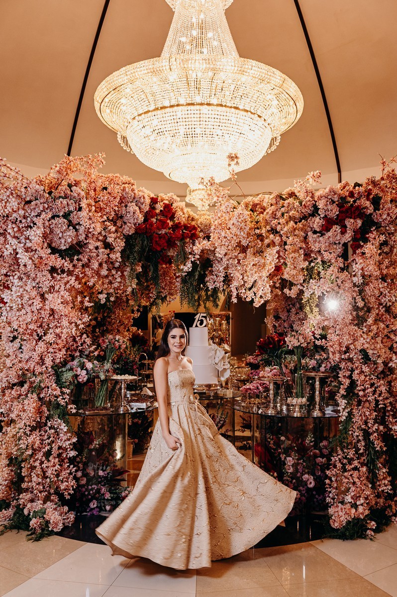 Foto da debutante em frente a mesa florida de doces