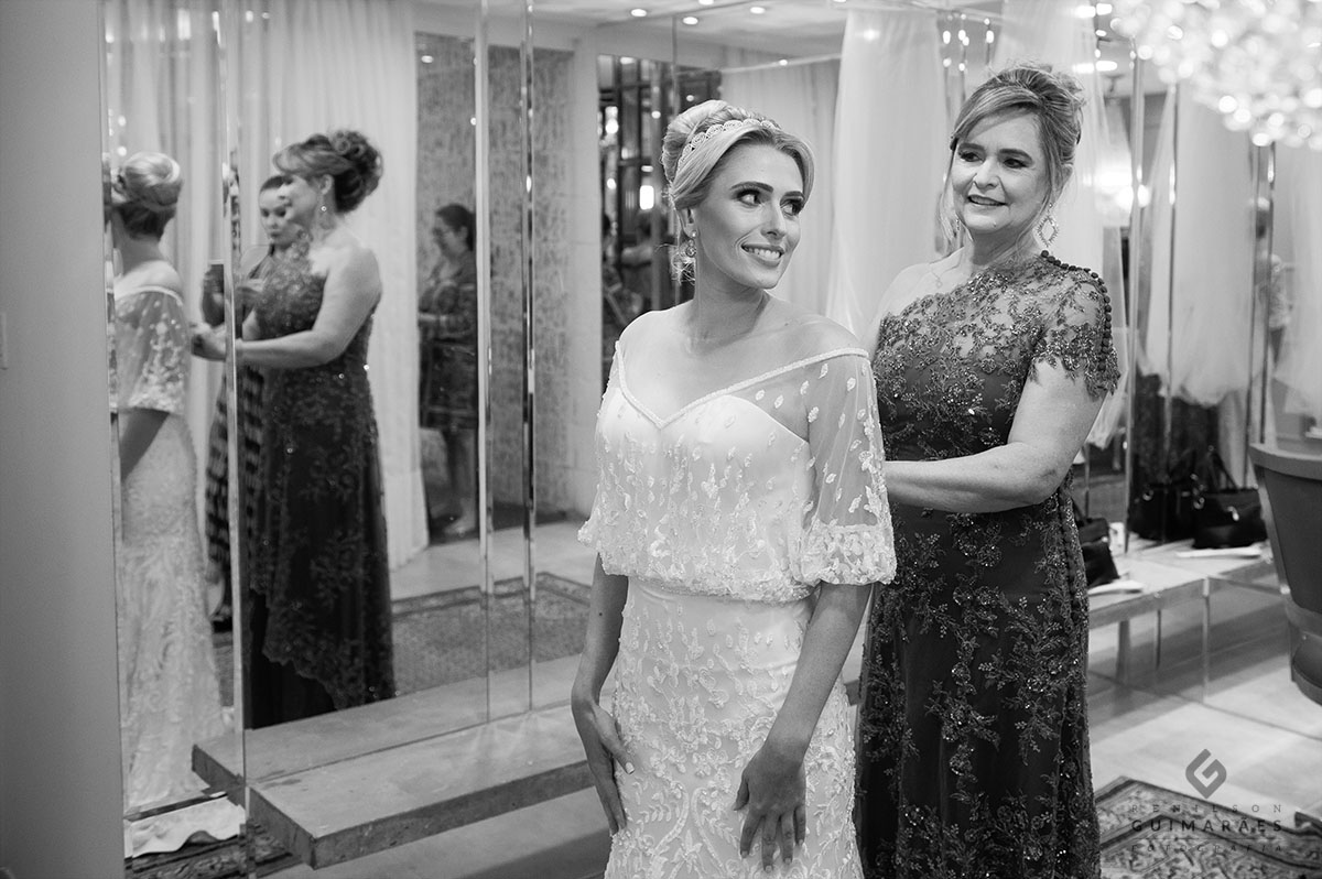 A mãe fechando o vestido da noiva