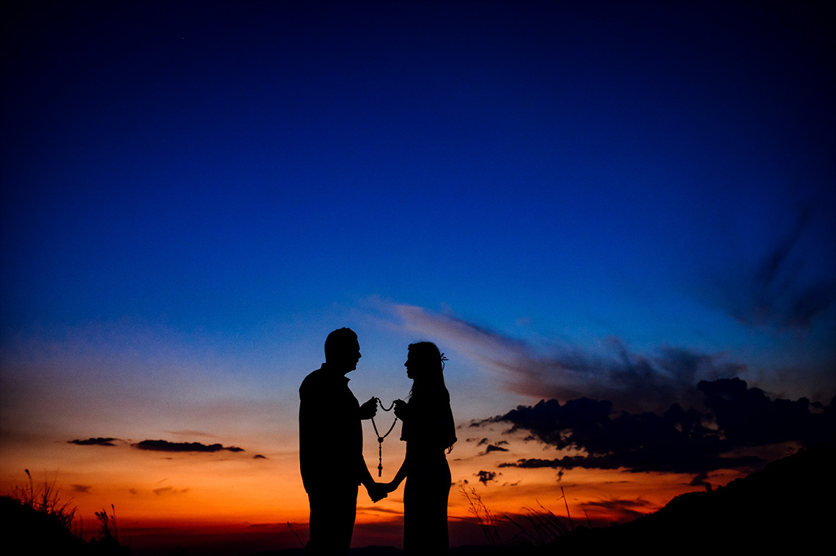 Silhueta dos noivos no por-do-sol com rosário