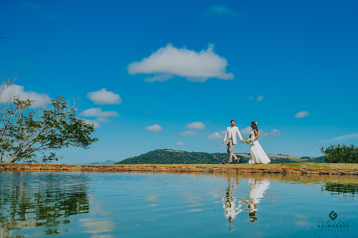 Noivos caminhando na beira do rio com reflexo na água