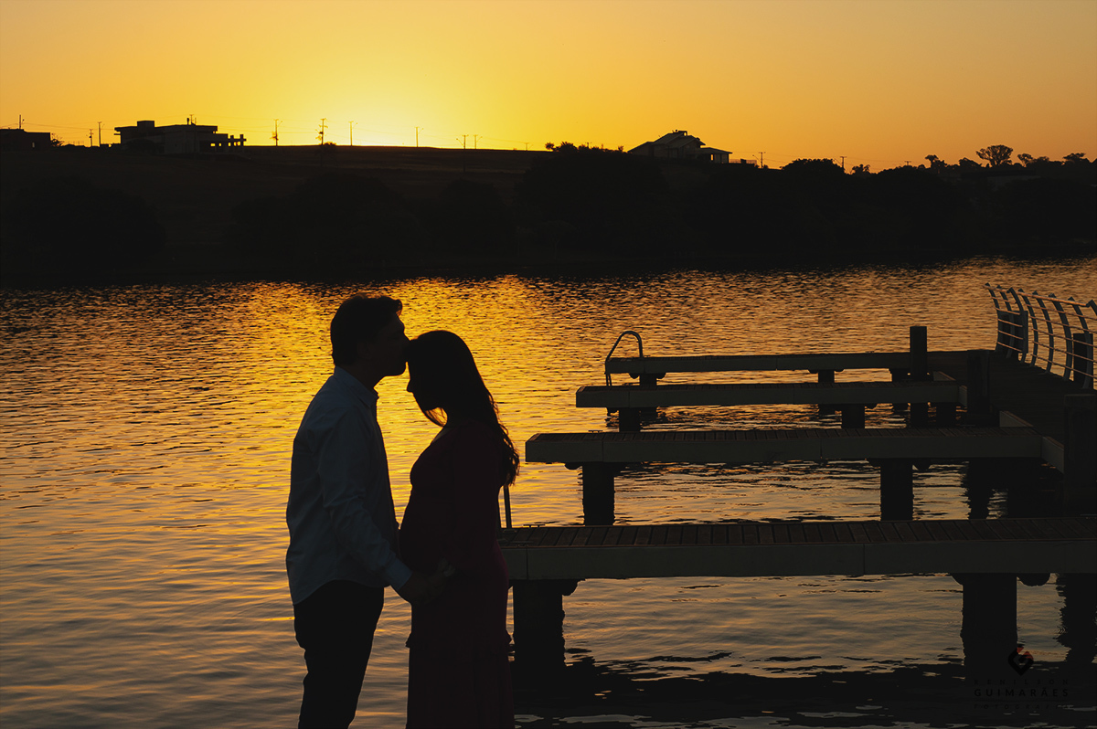 Foto no pôr-do-sol do pai do bebê beijando a testa da gestante 
