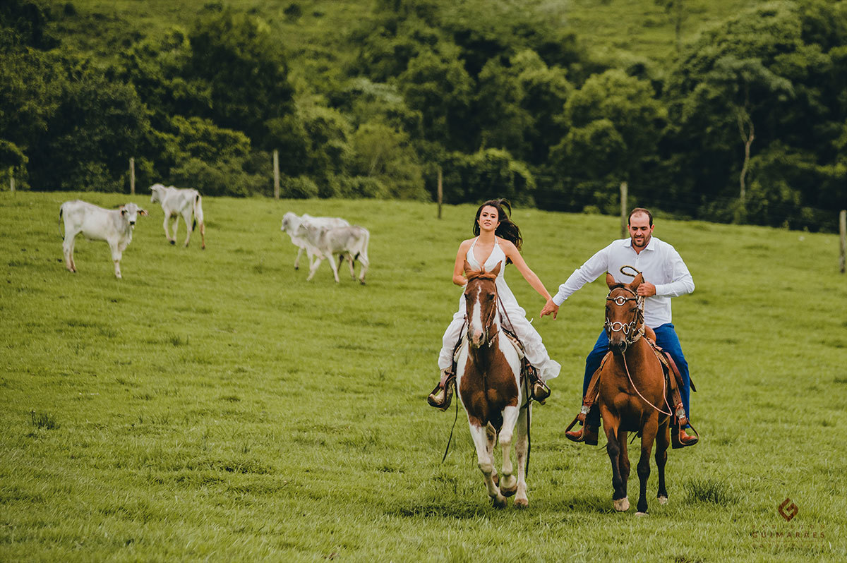Noivos de mãos dadas galopando no pasto