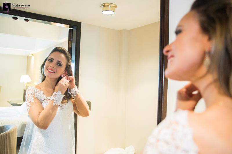 Noiva feliz coloca os brincos, sob as lentes de Giselle Solyom fotógrafa de casamento, de frente ao espelho.