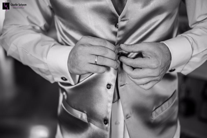 Detalhe das mãos do noivo abotoando o colete enquanto se veste para o seu casamento.