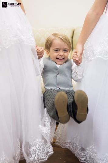 Menino de 3 anos muito feliz se pendura nas mãos das damas maiores, sorrindo enquanto espera para entrar no casamento em Igreja Santo Agostinho em Curitiba - PR