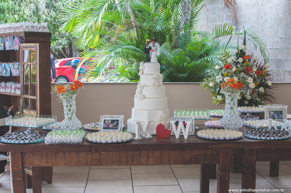 Decoração da mesa do bolo com docinhos e porta retratos com fotos do e-session do casal