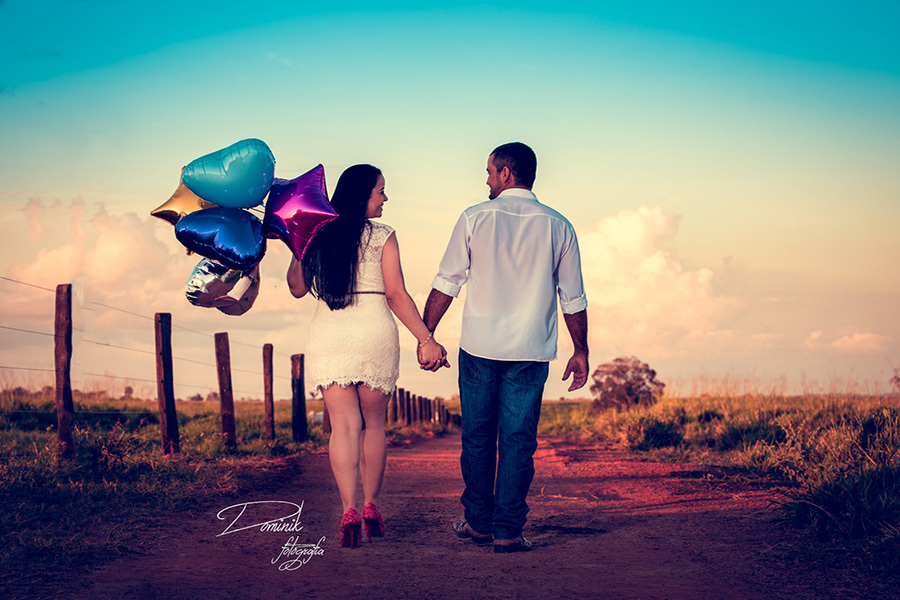 noivos passeando em uma estrada rural a noiva usando vestido curto branco e com balões na mão de maos dadas com o noivo por do sol cachoeira da serra ensaio pre casamento dominik fotografia