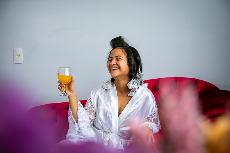 noiva no making of fazendo brinde sorrindo sentada num sofa vermelho colider sinop itauba guaranta mato grosso dominik fotografia album casamento