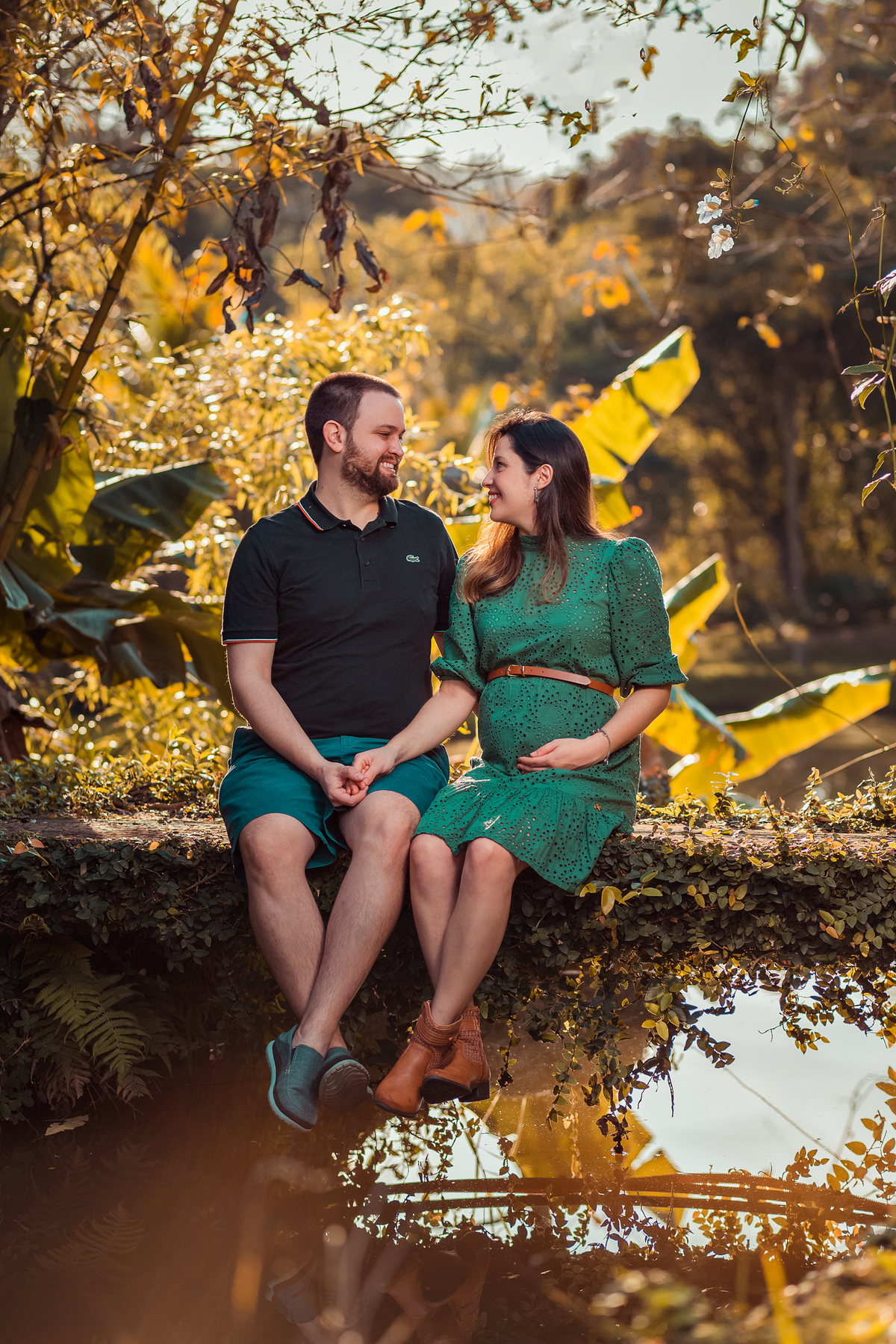 casal sentados trocando olhares de mãos dadas em ensaio externo de gestante 