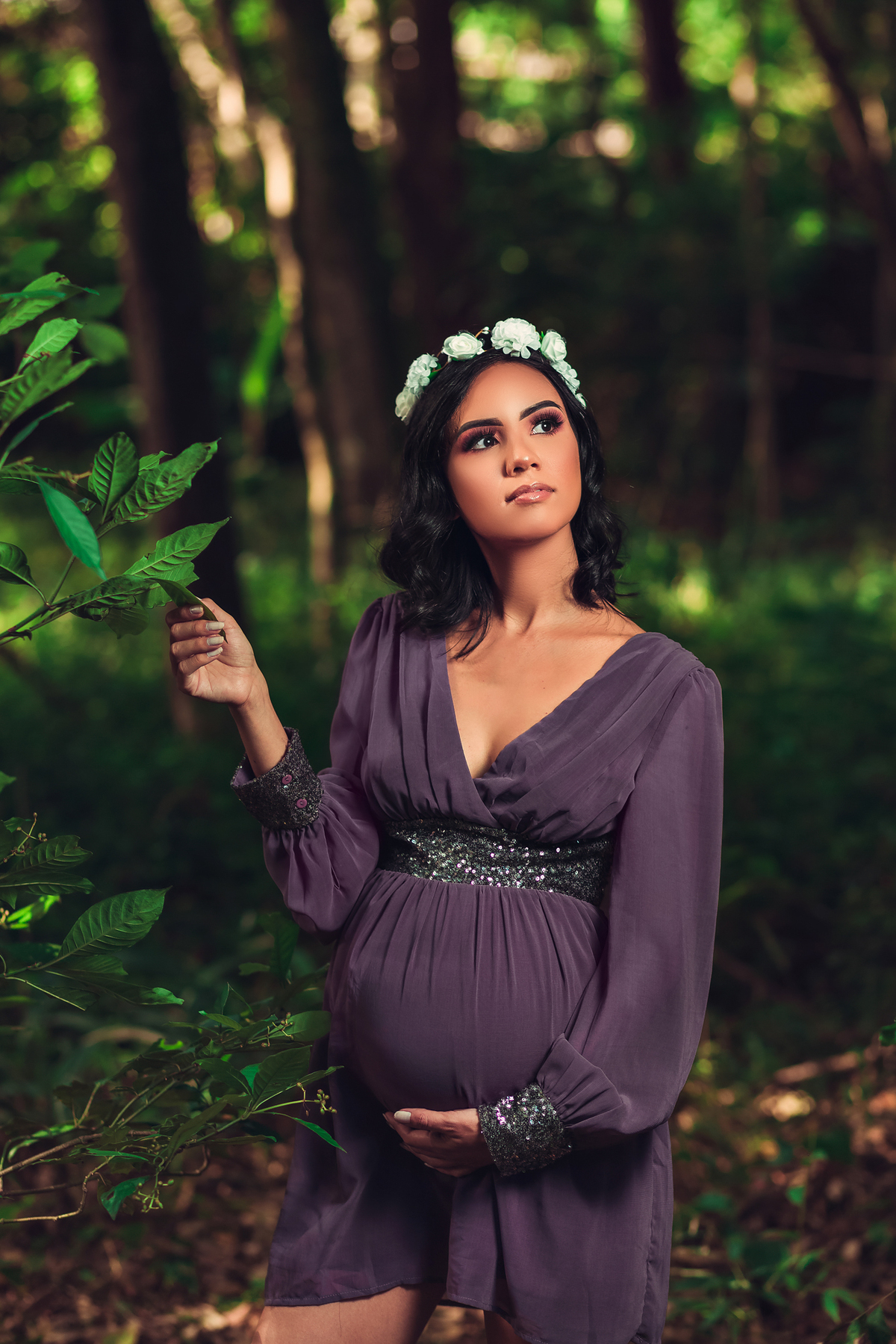 gestante com coroa de flores na cabeça segurando na folha em ensaio gestante