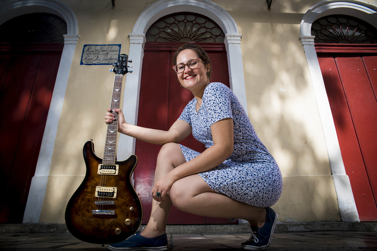 Mulher abaixada segurando uma guitarra em frente à Sinagoga no Recife Antigo, por Rafaelly Lemos