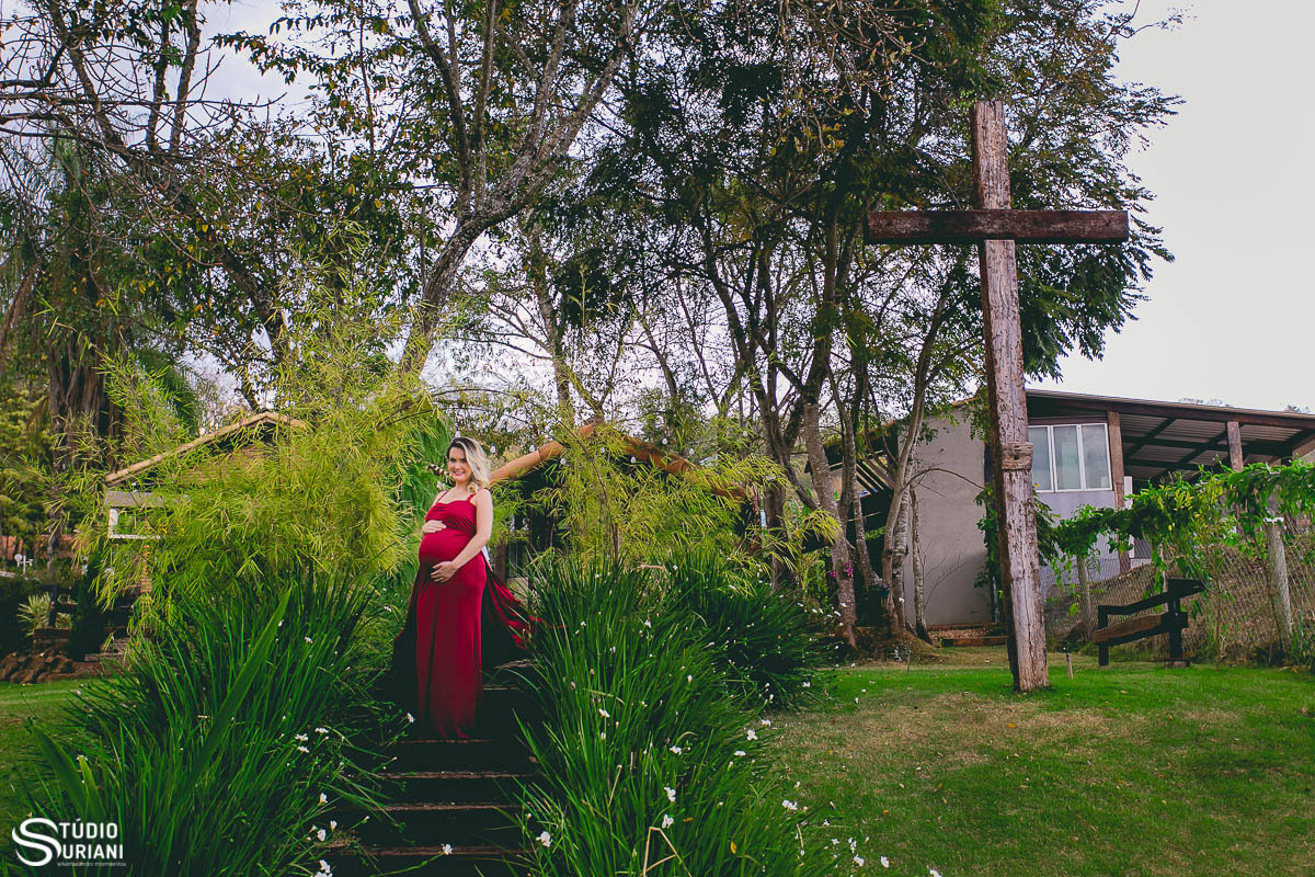 Fotos com vestido vermelho em chácara com uma grande cruz de Jesus cristo com jardim verde 