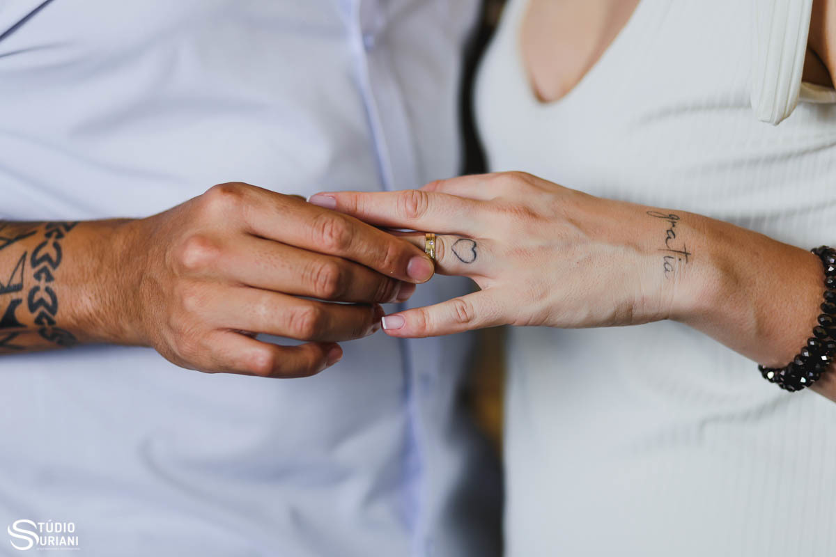 noiva com coração tatuado no dedo colocando a aliança de casamento 