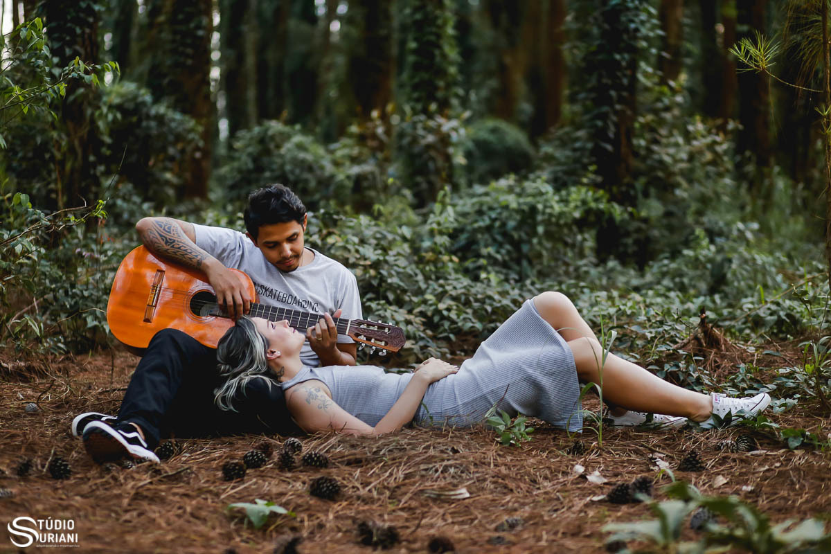 Noivo tocando seu violão que esta deitada em seu colo em floresta de pinhas em Uberlândia