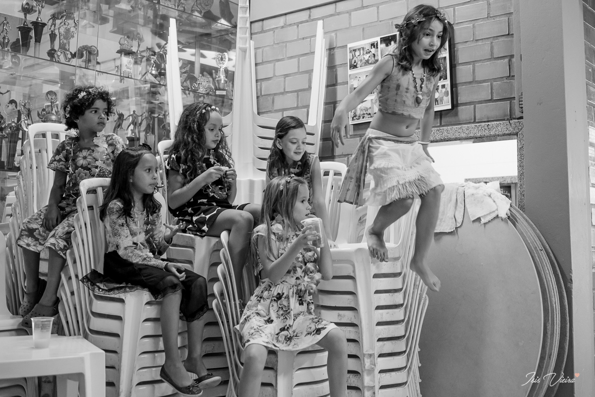 a aniversariante pula da cadeira em meio a brincadeira com suas amigas na sua festa de aniversario infantil realizada em florianopolis com registro da fotografa isis vieira