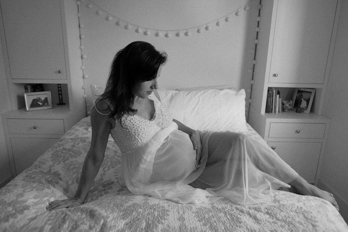 momento sereno da gestante flavia que olha com ternura para sua barriga e a acaricia com carinho em registro fotografico para o seu ensaio de gestante em florianopolis sc