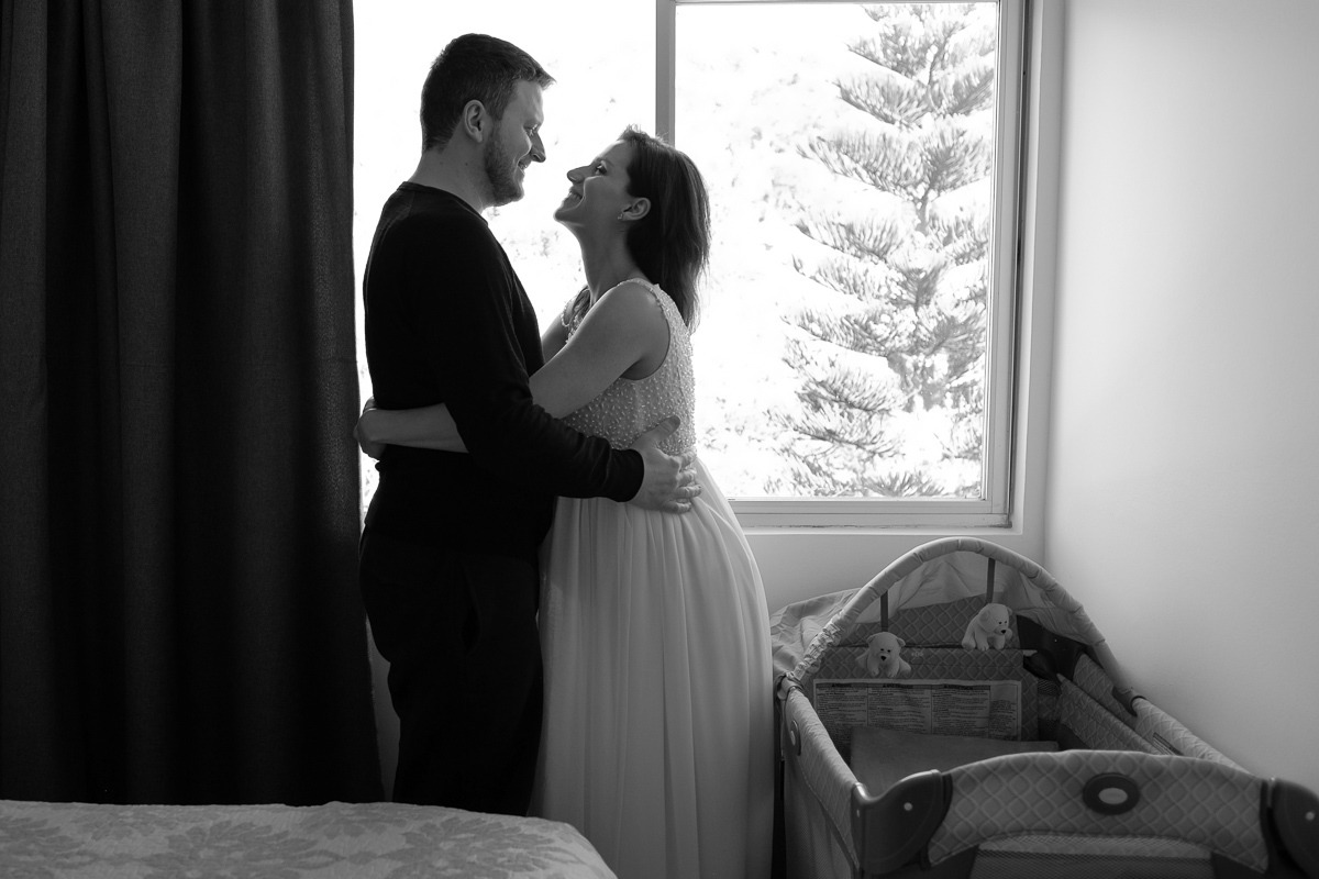 flavia e seu marido curtem um abraço cheio de amor e ternura no quarto do casal com o berço do bebê junto dos dois em ensaio de gestante realizado em casa no bairro do corrego grande em florianopolis sc