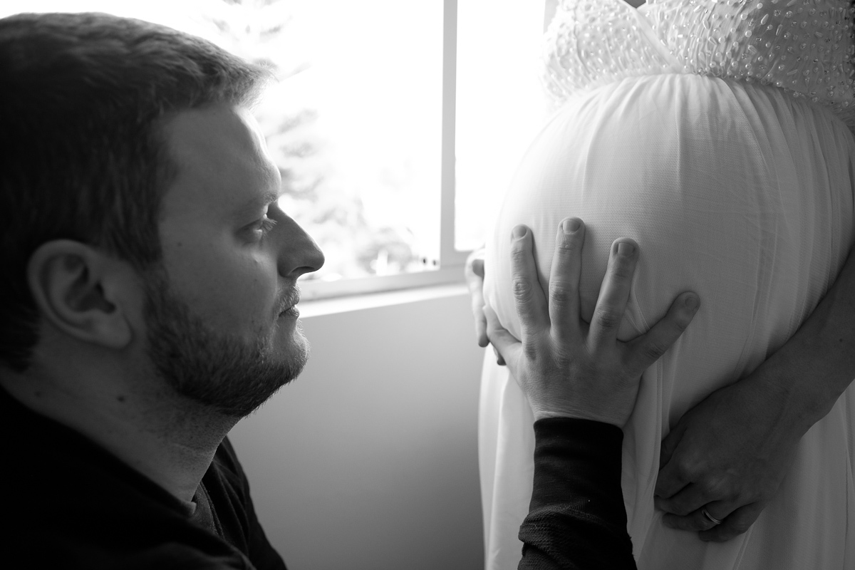 o pai olha e acaricia a barriga da mãe na linda espera do filho francisco em ensaio de gestante realizado na casa do casal em florianopolis sc