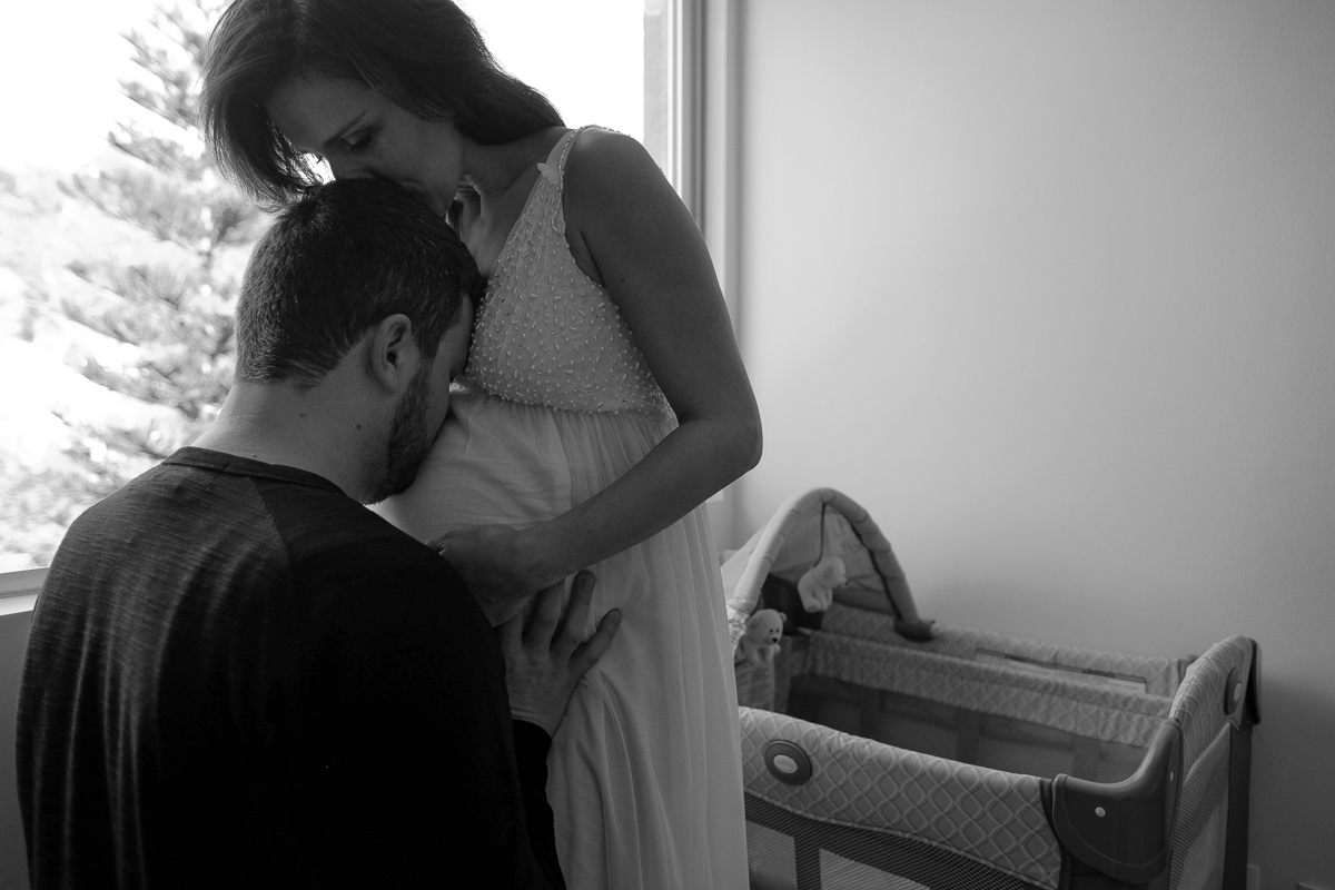 flavia beija a cabeça de seu marido e ele beija a sua barriga de gravida em lindo momento de carinho e amor no ensaio de gestante realizado na casa do casal e fotografado pela fotografa isis vieira em florianopolis sc