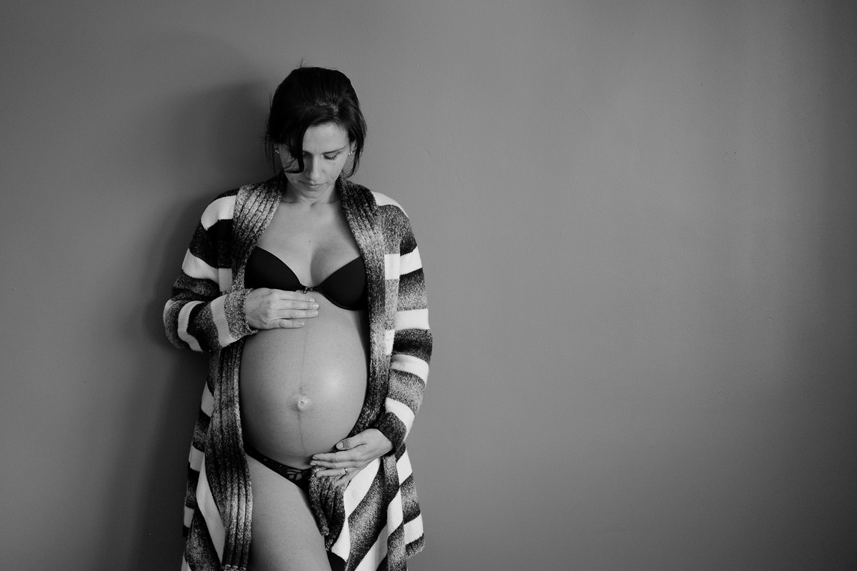 acariciando sua linda barriga de oito meses a gestante flavia posa na sua sala de estar para o seu ensaio de gestante fotografado pela fotografa de familias e infantil isis vieira fotografia